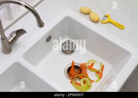 Vegetable scraps in kitchen sink with garbage disposal, above view Stock Photo