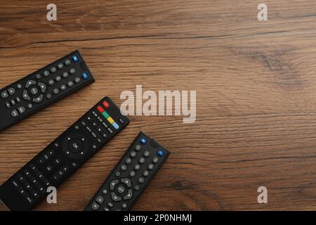 Modern tv remote controls on wooden table, flat lay. Space for text Stock Photo