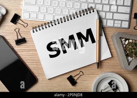 Notebook with abbreviation SMM, keyboard and smartphone on wooden table, flat lay. Social media marketing Stock Photo
