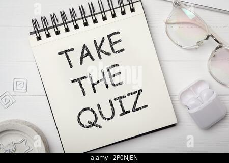 Phrase Take the quiz written in notebook on white wooden table, flat lay Stock Photo