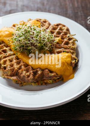 Plate with home made zucchini waffles, served with a vegan carrots based cheddar sauce. Stock Photo