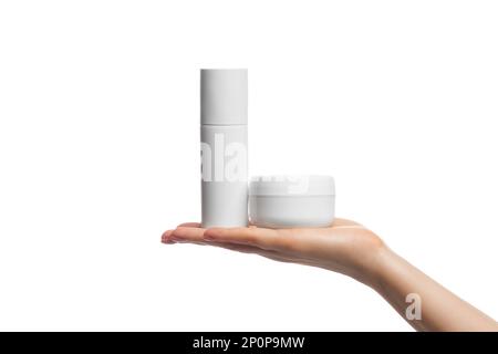 A couple of different white cosmetic containers on a woman's hand. Spray bottle an cream jar, isolated. Stock Photo