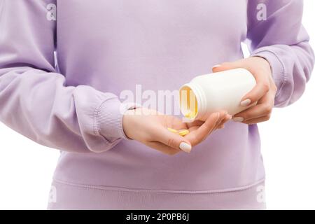 Cropped shot of a woman in a lavander oversized sweatshirt pours out yellow pills of the big white bottle. Stock Photo