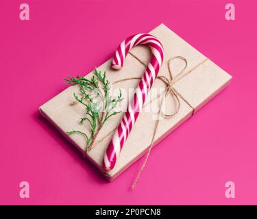 Gift wrapped in craft paper and candy cane on pink background. New Year or Christmas concept. Stock Photo