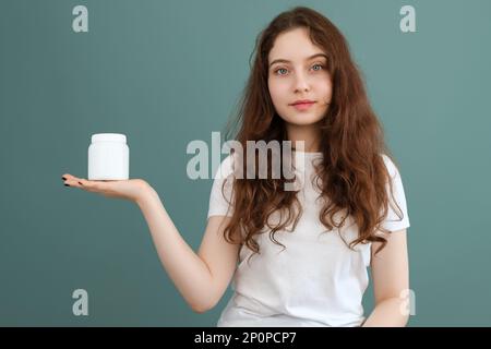 Beautiful brunette girl is holding a white jar with copy space, place for logo or advertisement. Stock Photo