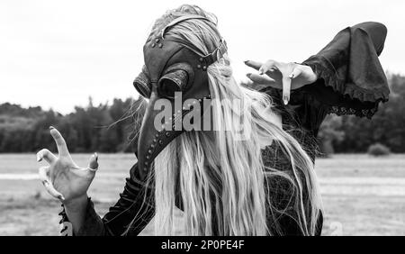 An eerie and surreal photo of a woman in a crow mask standing in a field. Black and white image Stock Photo