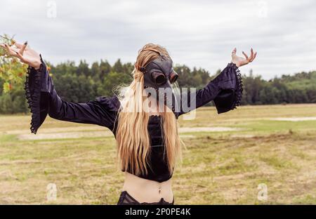 An eerie and surreal photo of a woman in a crow mask standing in a field. Stock Photo