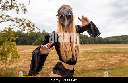 A fascinating and surreal photo of a woman in a crow mask amidst a field and forest. Stock Photo