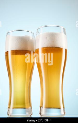 Fizzy yellow beer poured to tall glasses on light blue. Stock Photo