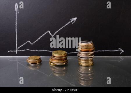 Coin stacks next to a ascending graph on a black chalk board. Close up Stock Photo