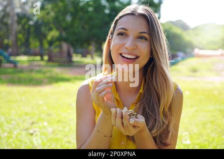 Attractive smiling healthy young woman eating Brazil nuts in park on summer Stock Photo
