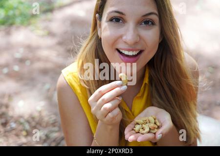 Beautiful healthy girl eating cashew nuts in the park. Looks st camera. Stock Photo