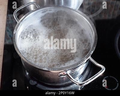 water boils in steel pan on ceramic stove in home kitchen Stock Photo