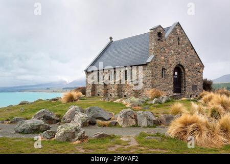 A majestic old stone church stands atop a grassy hill, overlooking a calm lake surrounded by lush greenery Stock Photo