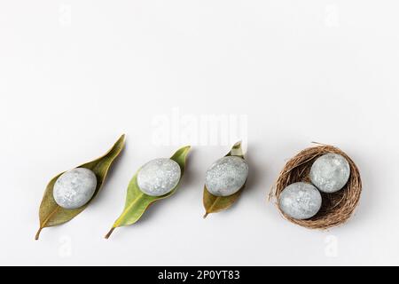 Minimal ecological Easter concept with dried flowers. Gray eggs on dry magnolia leaves and in a brown nest of twigs on a gray background. Copy space, Stock Photo