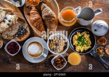Breakfast served with coffee, orange juice, scrambled eggs, cereals, pancakes and croissants. Stock Photo