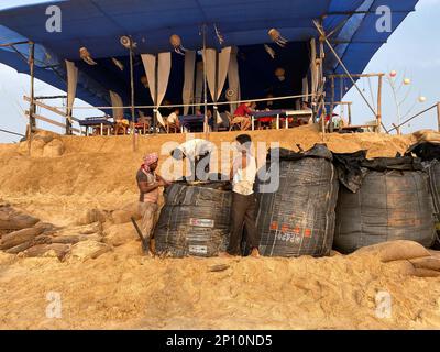 Candolim, Goa, India - January 2023: A team of workers filling sand bags outside a beach shack to prevent coastal erosion during high tide. Stock Photo