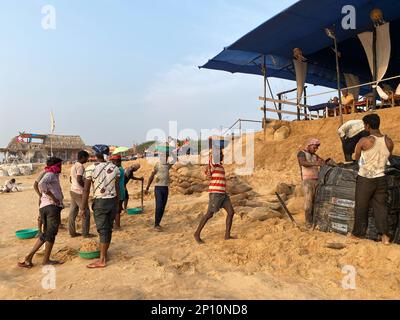 Candolim, Goa, India - January 2023: A team of workers digging the sand on a beach to protect seaside restaurants and prevent coastal erosion. Stock Photo