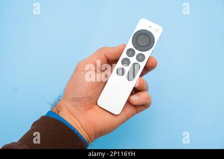 Mans hand holding Siri Apple TV remote controller on the blue background, February 2023, Prague, Czech Republic Stock Photo