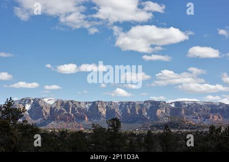 Snow on top of red rocks of Sedona, Arizona, with puffy white clouds in a blue sky. Stock Photo