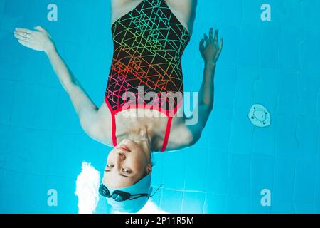 Top view of a young female swimmer training in the pool, swimming on her back underwater. Floats under water and blows air rings Stock Photo