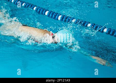 Beautiful female swimmer using front bypass, freestyle in the pool. Preparing professional athletes to win the championship. Stock Photo