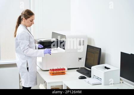 Woman doctor stands near a hematological analyzer in testing unit Stock Photo