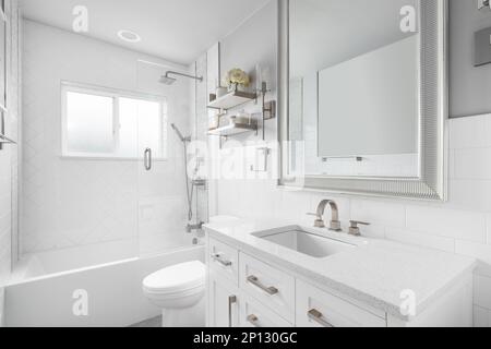 A bathroom with a white vanity cabinet, granite countertop, and a shower lined with large herringbone tiles. Stock Photo