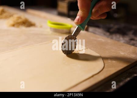 Cook cutting dough with cutter tool. Italian chef cooking pasta in the kitchen Stock Photo