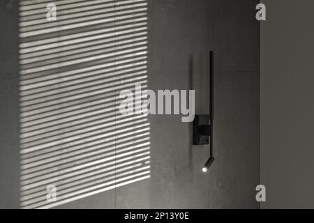 Minimalistic black wall light in modern interior in grey and black colours, concrete wall design, clay wall. Contemporary interior design aesthetics w Stock Photo