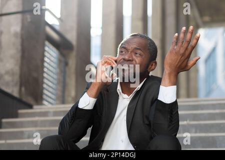Losing the case in court. Upset scared black man sitting on steps outside courthouse. Talking on the phone. Divorce, alimony, custody, bankruptcy, deportation. Stock Photo