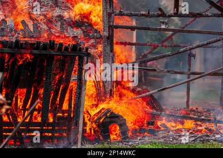 Wooden barn with doghouse in front completely consumed by fire is burnt to the ground. Close-up of a burst of fire coming from a burning barn. Stock Photo