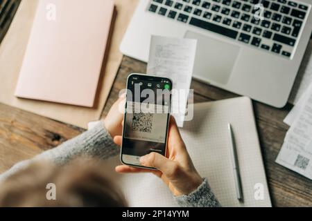 An unrecognizable woman works with bills using a qr code reader app on a mobile phone. Stock Photo