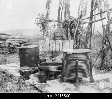 Ainu man seated outdoors on a mat covered with clay containers, 1908. Stock Photo