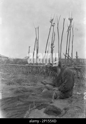 Ainu seated outside working on nets, 1908. Stock Photo