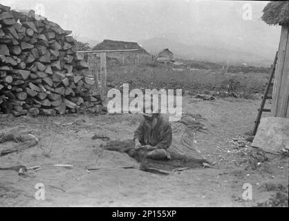 Ainu man seated outside working on nets, 1908. Stock Photo