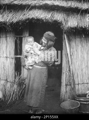 Ainu woman holding a child standing outside a hut, 1908. Stock Photo