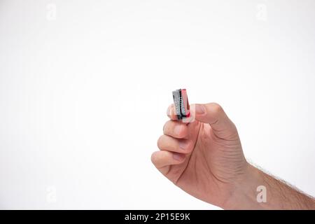 Caucasian male hand holding an old CR123A type battery between fingers. Close up studio shot, isolated on white background. Stock Photo