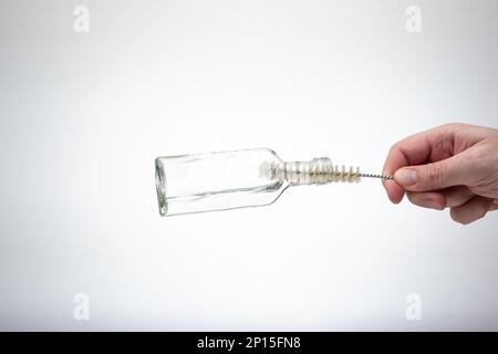 Cleaning an empty glass bottle with a small wire brush. Male hand holding the brush. Close up studio shot, isolated on white background. Stock Photo