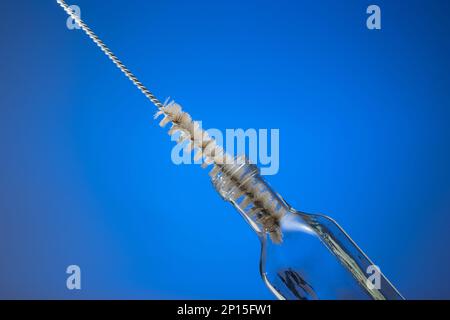 Thin wire brush for cleaning bottles. Inside small empty glass bottle. Close up studio shot, isolated on blue background. Stock Photo