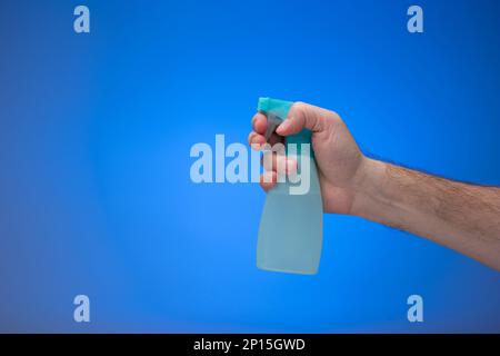 Light blue water sprayer bottle nozzle held by male hand. Close up studio shot isolated on a blue background. Stock Photo