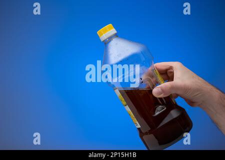 Spent cooking oil recycling in a clear plastic bottle. Held in hand by man. Close up studio shot, isolated on blue background. Stock Photo