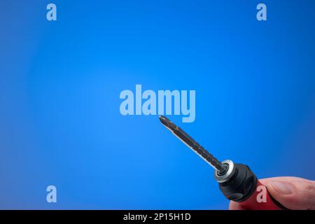 Turn screwdriver in man's hand. Close up studio shot, isolated on blue background. Stock Photo
