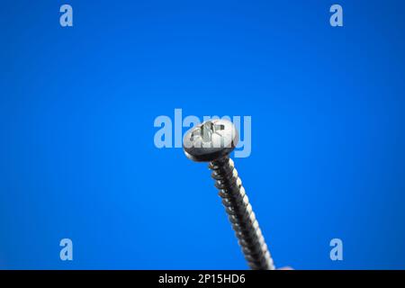 Small metal threaded screw. Close up studio macro shot, isolated on blue background. Stock Photo