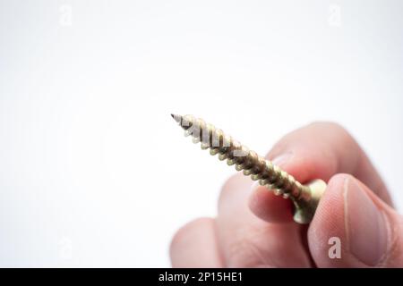 Small metal threaded screw held by Caucasian male hand between fingers. Close up studio macro shot, isolated on white background Stock Photo