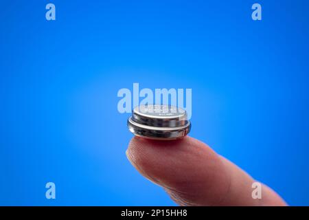 Caucasian male hand holding a button type battery between fingers. Close up studio shot, isolated on white background. Stock Photo