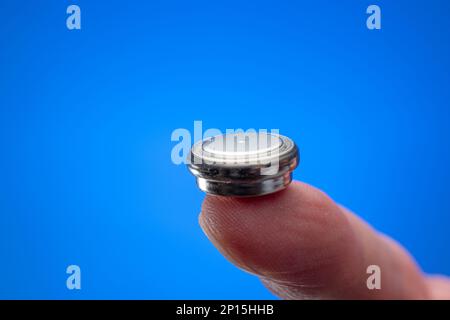 Caucasian male hand holding a button type battery between fingers. Close up studio shot, isolated on white background. Stock Photo