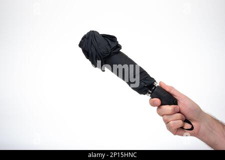 Folded and closed black fabric umbrella held in hand by man. Close up studio shot, isolated on white backgroun. Stock Photo