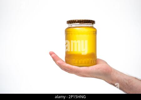 Fresh golden yellow bee honey in a glass jar, held by Caucasian male hand. Close up studio shot, isolated on white background. Stock Photo