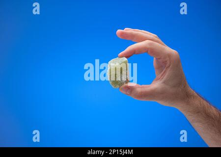 Cube of delicious green colored Turkish Delight held in male hand. Close up studio shot, isolated on blue background. Stock Photo